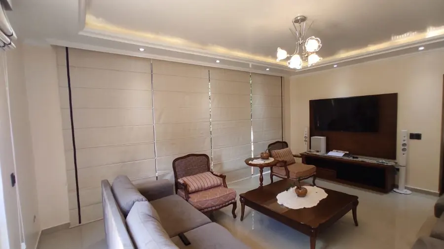 Cortina romana en una sala con sillones y mueble para el televisor
